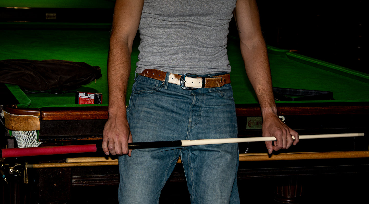 Person wearing a cowhide print belt holding a pool cue in front of a pool table