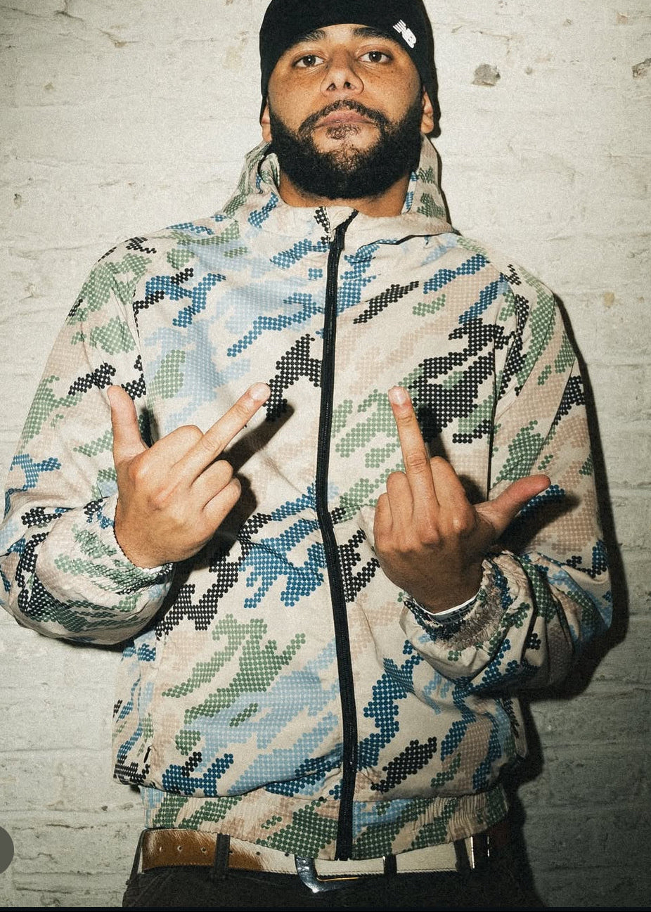 Person wearing a camouflage jacket wiith a cowhide leather belt making hand gestures against a textured wall.
