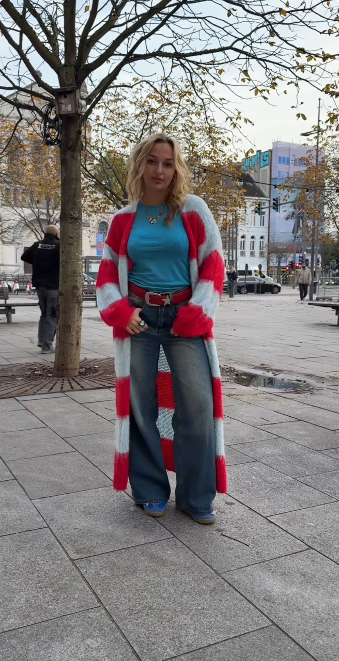 A woman wearing a colourful cardigan with a red belt on a city street