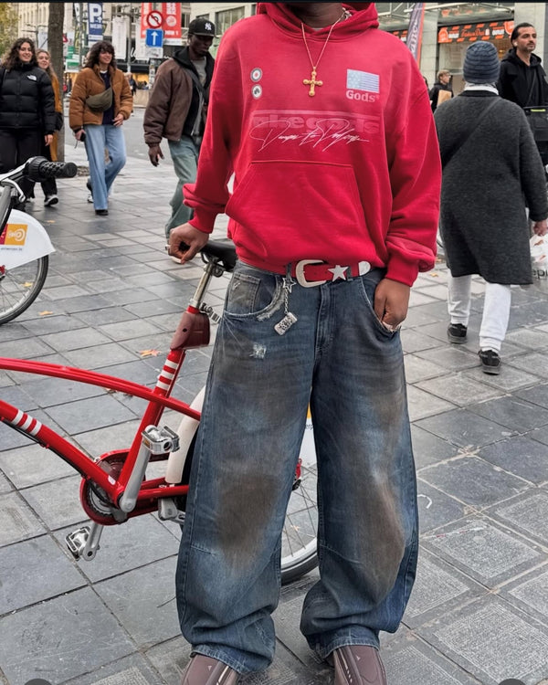 Person wearing a red hoodie and blue jeans standing on a street with a bicycle.