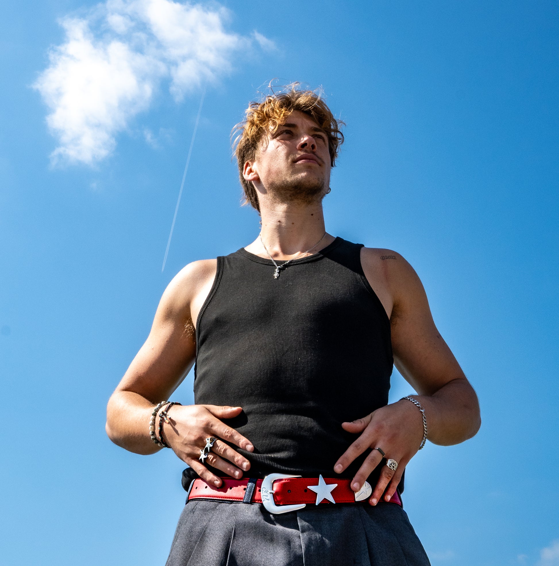 Man wearing a black tank top and red belt with a star against a blue sky