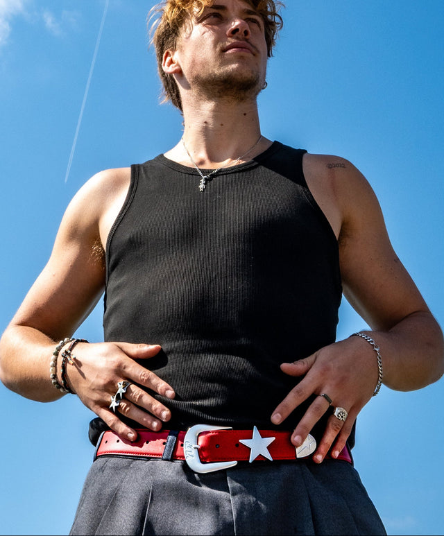Man wearing a black tank top and red belt with a star against a blue sky
