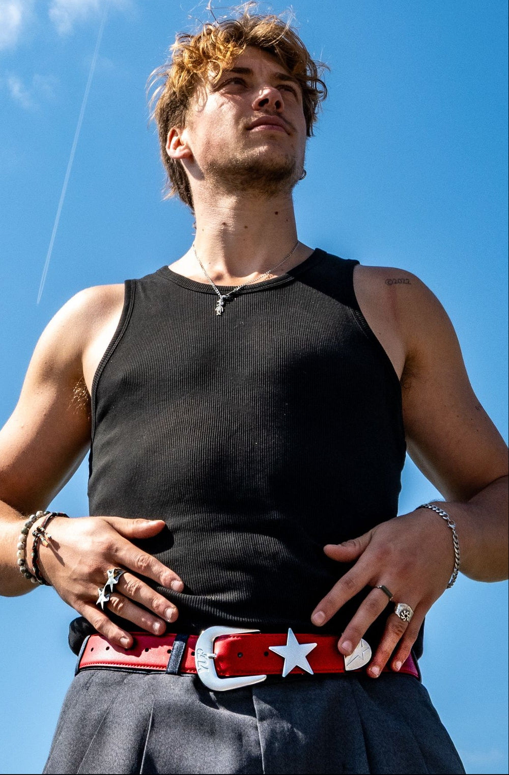 Man wearing a black tank top and red belt with a star against a blue sky